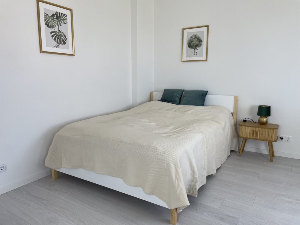 Nahaufnahme Schlafbereich mit Bett, Nachttisch und Wandbild Zeigt: helles Holzbett,Nachttisch, botanische Bilder an der Wand
