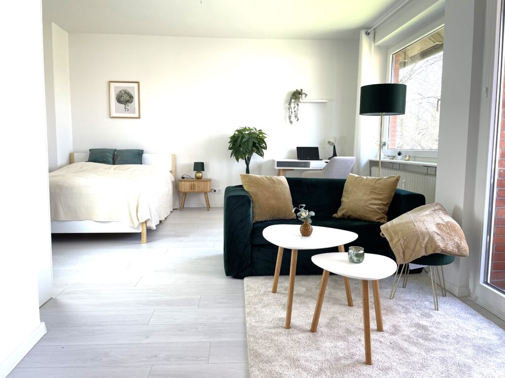Nacher Einrichtung Blick vom Wohnbereich in den Schlafbereich & Schreibtisch: Sofa und Bett klar getrennt, ohne eine einzige Trennwand. Zonierte Einzimmerwohnung
