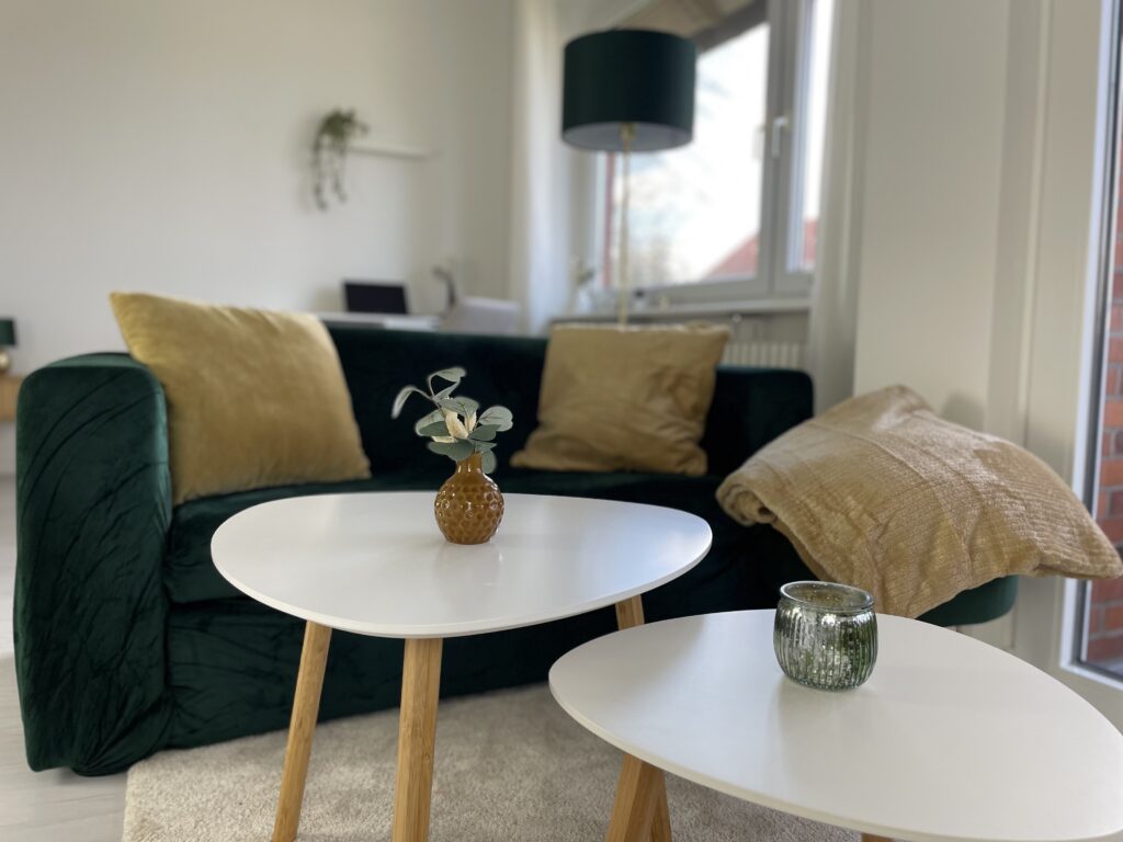 nahaufname sofaecke mit dunkelgrünem Samtsofa, senffarbenen Kissen und Couchtische im Scandistil mit Farbakzenten