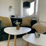 nahaufname sofaecke mit dunkelgrünem Samtsofa, senffarbenen Kissen und Couchtische im Scandistil mit Farbakzenten